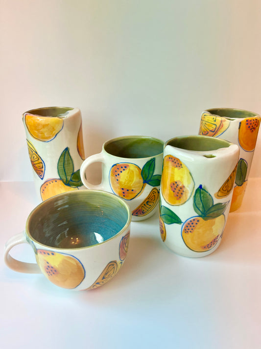 Several different handmade pottery mugs with oranges and green leaves.