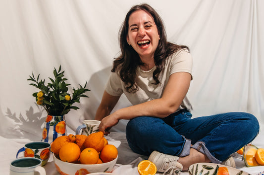 a woman laughing while surrounded by orange themed pottery with a bowl full of oranges.