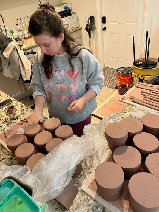 Female with long black hair cutting pottery clay in her in house studio.