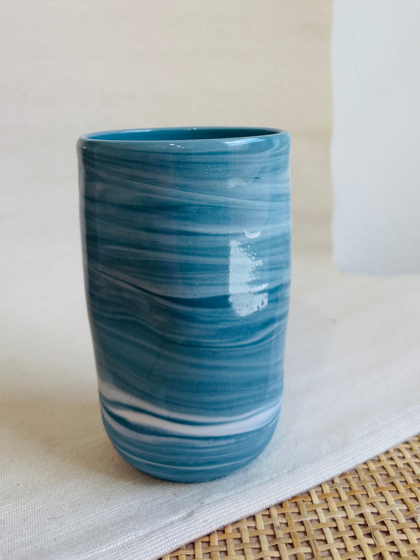 Blue ceramic tumbler on a light surface with a woven mat underneath