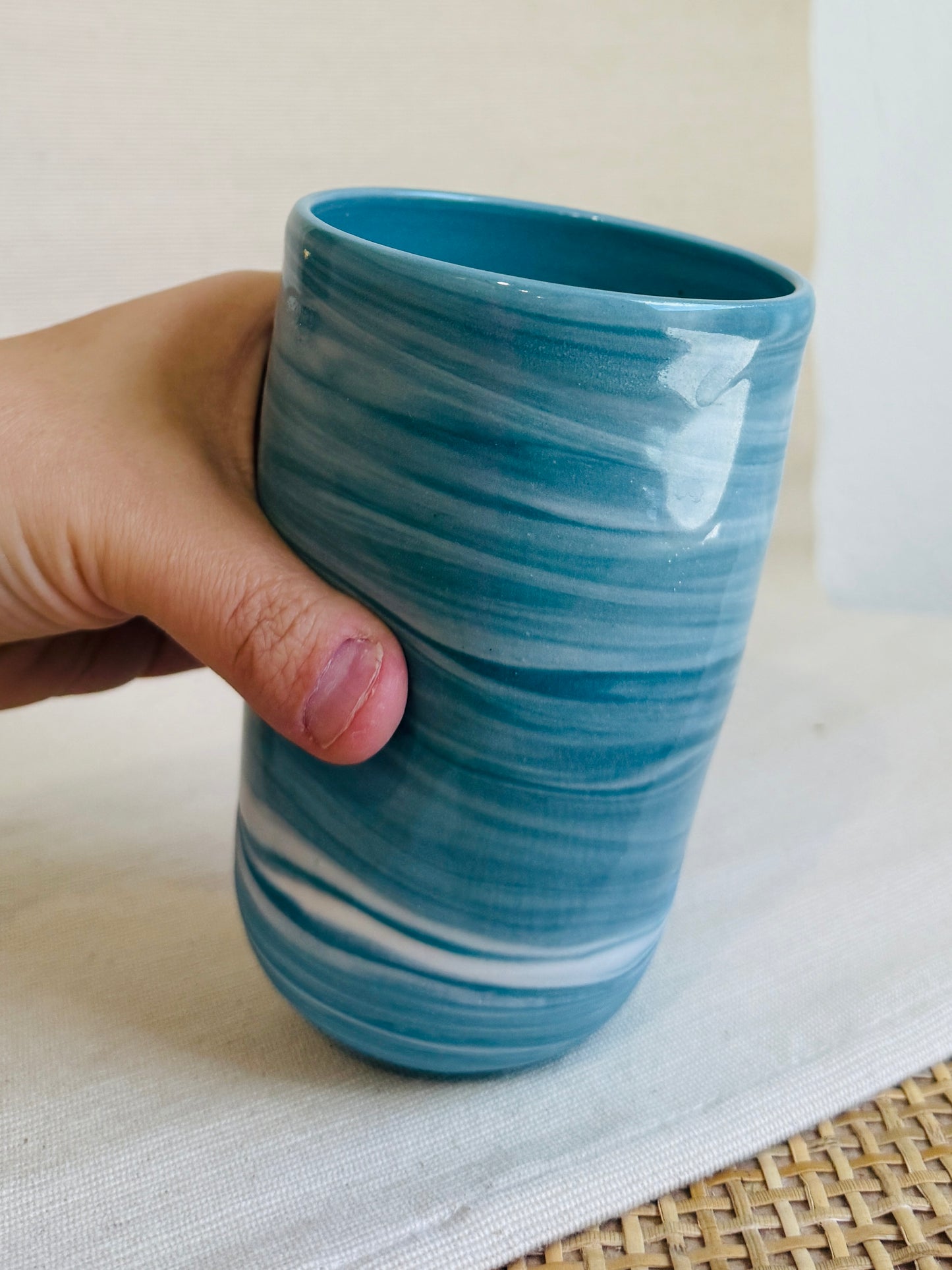 Hand holding a blue ceramic cup with white swirl patterns on a light background