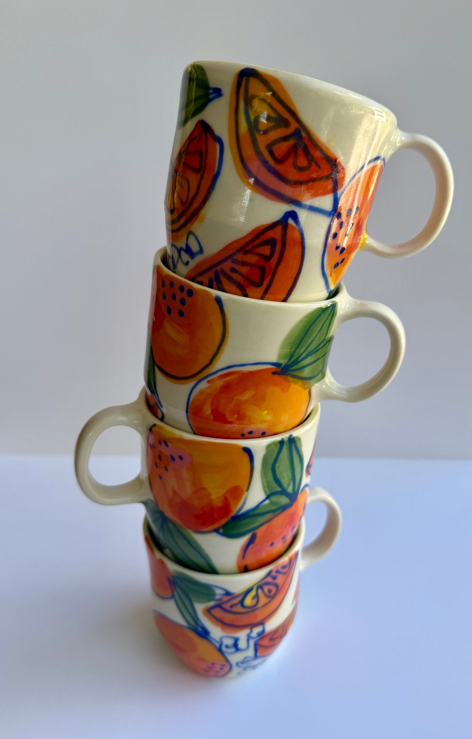 stacked mugs with oranges, orange slices, and blue outline drawings of orange blossoms