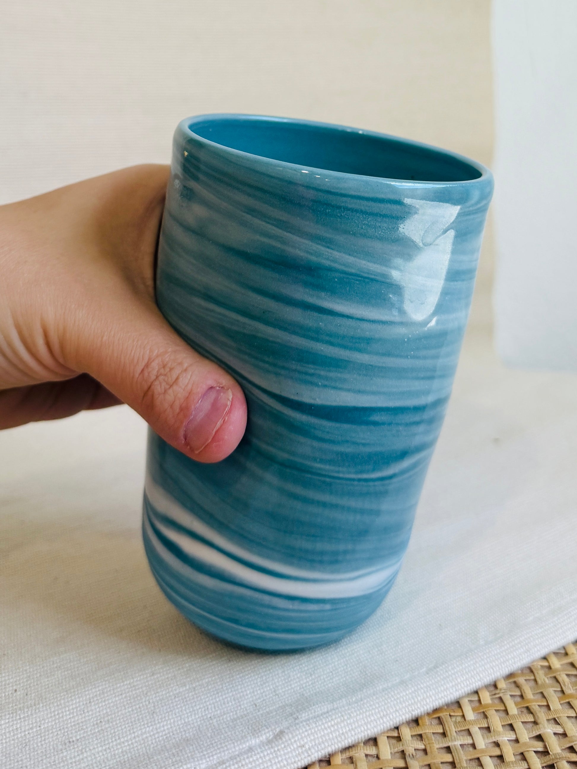 Hand holding a blue ceramic cup with white swirl patterns on a light background